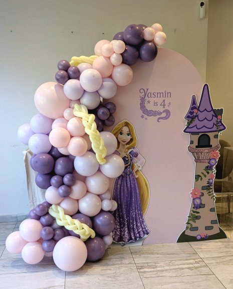 Rapunzel birthday decoration with pastel purple and pink balloons, tower cutout, and yellow balloon braid detail