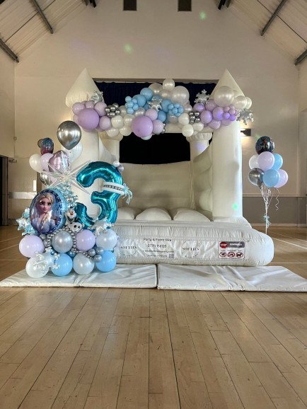 Bouncy castle with Frozen themed balloon garland, Elsa balloon bouquet, co-ordinating helium filled clusters in shades of blue, lilac, silver and white.